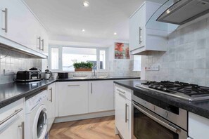 Una cocina moderna con armarios blancos, lavadora integrada, estufa y ventana con vistas al exterior.