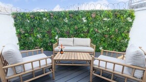 A wooden deck with a white sofa and two chairs, a bottle of wine, and a green vertical garden wall. - Large Period 2-Bed Apartment Close to Town (Gloucestershire)