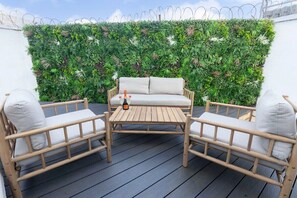 Une terrasse en bois avec un canapé blanc et deux fauteuils, une bouteille de vin et un mur végétal vertical.