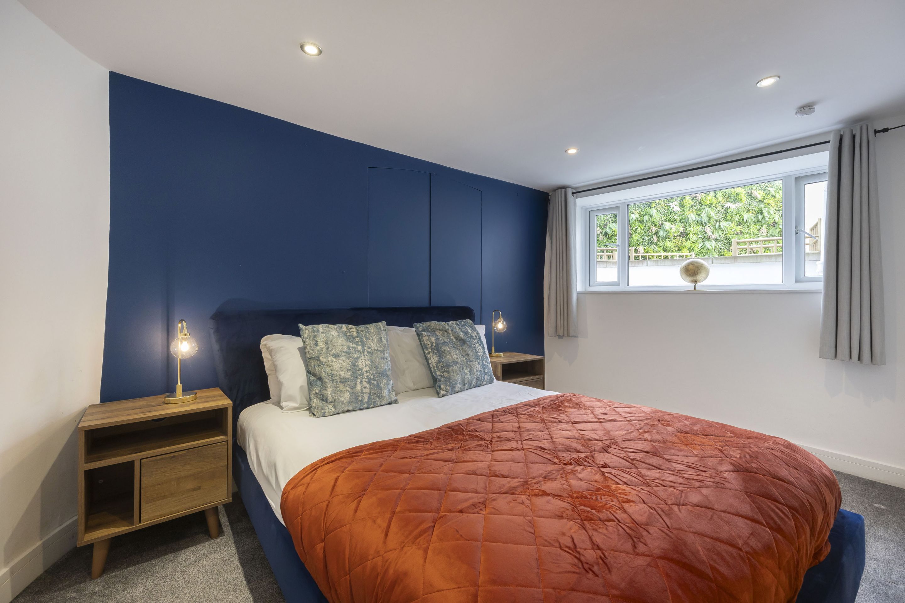 Un dormitorio con cama, mesitas de noche, una ventana y vistas al exterior.