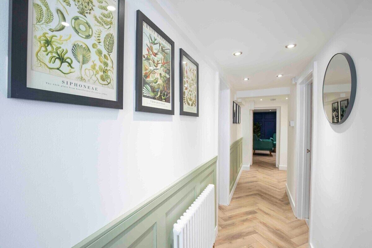 A hallway with framed botanical prints on the wall, a radiator, and a mirror on the right.