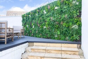 Een terras op het dak met een houten terras, buitenmeubels en een weelderige verticale tuinwand.