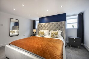 Een moderne slaapkamer met een groot bed, een nachtkastje, een spiegel en een raam met gordijnen.