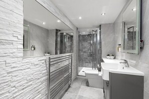 A modern bathroom with a glass shower enclosure, a standalone bathtub, and a vanity with a sink and mirror.
