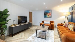 A modern living room with a sofa, a coffee table, a TV on a cabinet, and a painting on the wall. - Large Period 2-Bed Apartment Close to Town (Gloucestershire)
