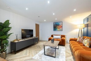 Un salon moderne avec un canapé, une table basse, un téléviseur posé sur un meuble et un tableau accroché au mur.