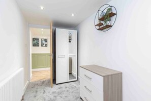 Una habitación con un armario blanco, un pequeño aparador de madera y una repisa para plantas en la pared.