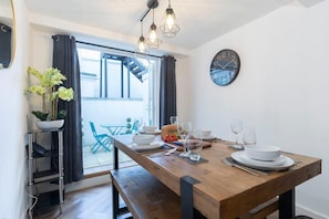 A dining area with a wooden table set for four, a black wall clock, and a potted plant.