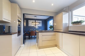 Una cocina moderna con armarios blancos, horno empotrado y una zona de comedor con mesa y sillas.