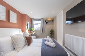 Une chambre d’hôtel avec un lit, un bureau, une plante en pot et un téléviseur fixé au mur.