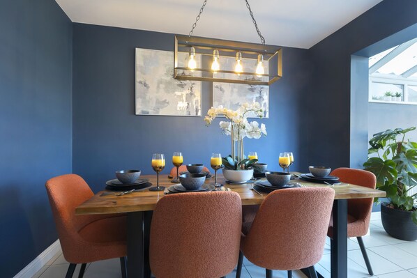 Un coin repas avec une table en bois, des chaises orange et un luminaire suspendu au design moderne.