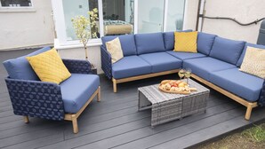 Un área de estar al aire libre con un sofá seccional azul y un sillón más pequeño, ambos con cojines estampados.