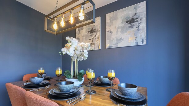 Comedor con mesa de madera dispuesta para cuatro personas, rodeado de sillas color naranja.