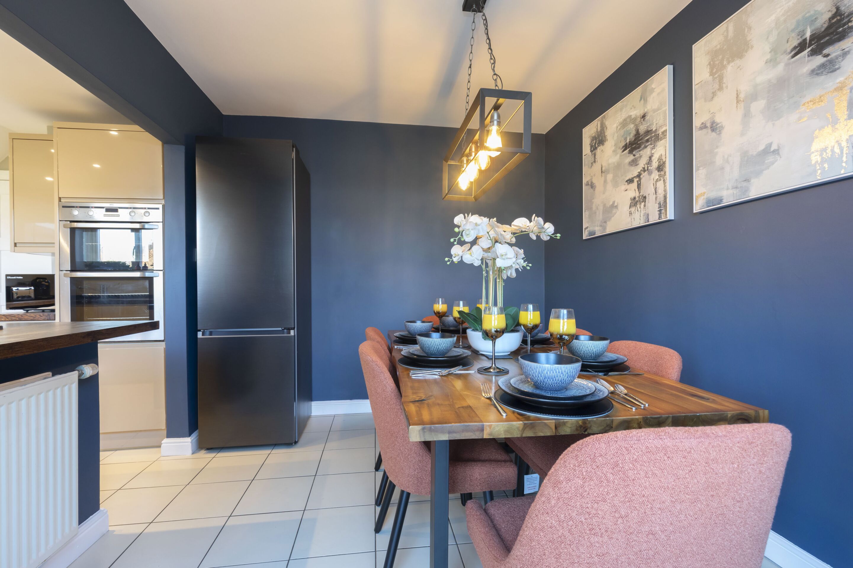 Een moderne keuken met een inbouwoven en koelkast, een eettafel gedekt met borden, kommen en glazen, en een vaas met witte bloemen.