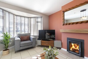 Una sala de estar moderna con un sofá gris, un televisor de pantalla plana, una chimenea y ventanas grandes con persianas.