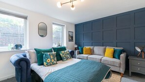 Ein Schlafzimmer mit einem Bett, zwei Sofas, einem Schminktisch und einem Spiegel, mit Fenster und Blick auf eine Backsteinmauer.