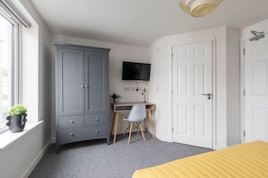 A bedroom with a bed, a desk, a chair, a wardrobe, and a TV.