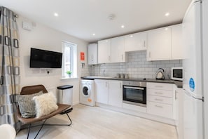A modern kitchen with white cabinets, a washing machine, an oven, and a microwave.