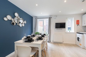 A modern kitchen with a dining area, a washing machine, and a TV.