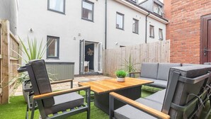 Eine Terrasse mit einem Holztisch, grau gepolsterten Stühlen, einem kleinen Topfpflanzen und einem grauen Sofa.