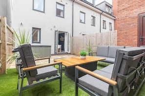 A patio with a wooden table and grey cushioned chairs, a small potted plant, and a grey sofa.