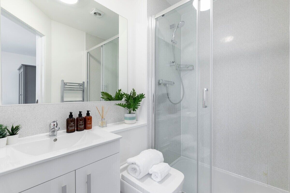 A modern bathroom with a glass shower enclosure, a white sink with toiletries, and a potted plant.