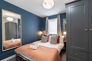 A bedroom with a bed, a wardrobe, a mirror, and a window with curtains.