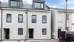 Ein modernes Wohnhaus mit zwei Etagen, Flachdach und zahlreichen Fenstern. Vor dem Haus ist ein schwarzer Van geparkt.