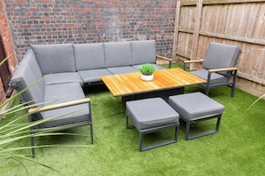 A sectional sofa, two armchairs, a coffee table, and two ottomans arranged on artificial grass. - Modern 4 Bedroom 4 Bathroom Home in Cheltenham (Cheltenham)