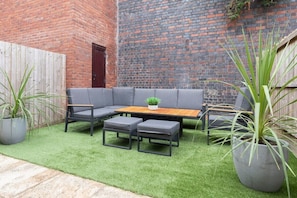 A cozy outdoor seating area with a sofa and two chairs, a wooden table, and two square ottomans. - Modern 4 Bedroom 4 Bathroom Home in Cheltenham (Cheltenham)