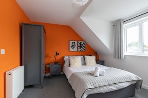 A bedroom with a sloped ceiling, an orange accent wall, a bed with white bedding, two bedside lamps, and artwork on the wall.