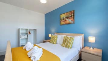 A hotel room with a bed, a nightstand, a bedside table, a wardrobe, and a painting on the wall.