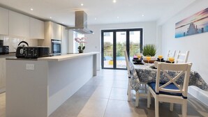 A modern kitchen with white cabinetry, a central island, and a dining area with a table set for four. - Modern & Spacious Home in Central Cheltenham (Gloucestershire)