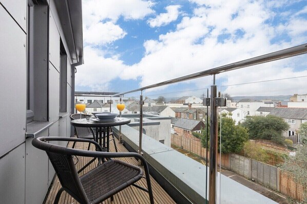 A balcony with a table and chairs, overlooking a residential area with houses and a clear sky.