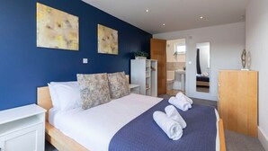 A modern bedroom with a large bed, two wall art pieces, a wooden wardrobe, and a bathroom visible through an open door. - Modern & Spacious Home in Central Cheltenham (Gloucestershire)