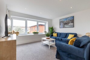 A modern living room with a blue sofa, a coffee table, and a large window with a view of buildings.