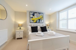 A bedroom with a bed, two bedside tables, a wall-mounted painting, and a window with blinds.
