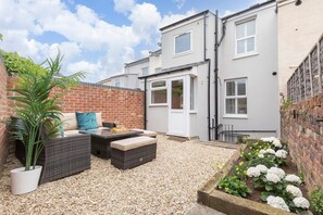 A residential property with a patio area featuring wicker furniture, a potted plant, and a flower bed.