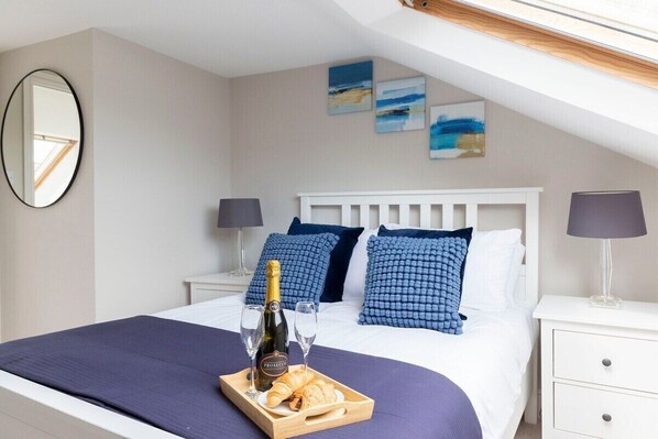 A neatly made bed with a white headboard, blue pillows, and a tray with a bottle and croissant.