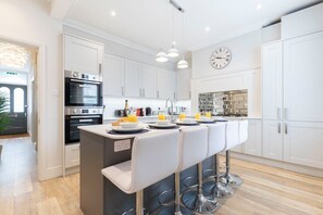 A modern kitchen with white cabinetry, a central island with bar stools, stainless steel appliances, and pendant lighting.