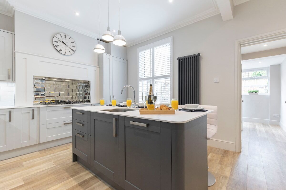 A modern kitchen with a central island, a built-in oven, and a large window with blinds.