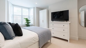 A bedroom with a bed, a TV on a dresser, and a window with blinds. - Stunning 5 Bed Regency Home (Gloucestershire)