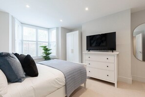 A bedroom with a bed, a TV on a dresser, and a window with blinds. - Stunning 5 Bed Regency Home (Gloucestershire)