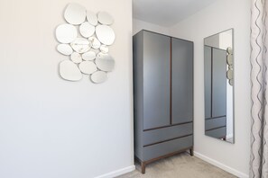 A room with a grey wardrobe, a wall-mounted mirror, and a decorative circular mirror arrangement.