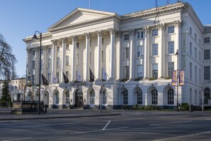 Un edificio grande de estilo clásico con columnas y ventanas arqueadas, con la leyenda “The Queen's Hotel”.