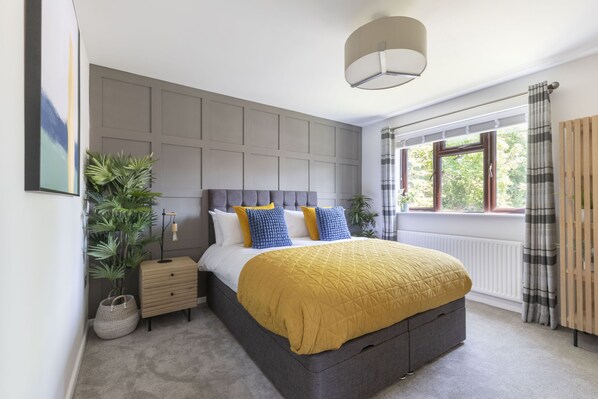Un dormitorio moderno con una cama grande, una mesita de noche, una lámpara de pie y una ventana con cortinas.
