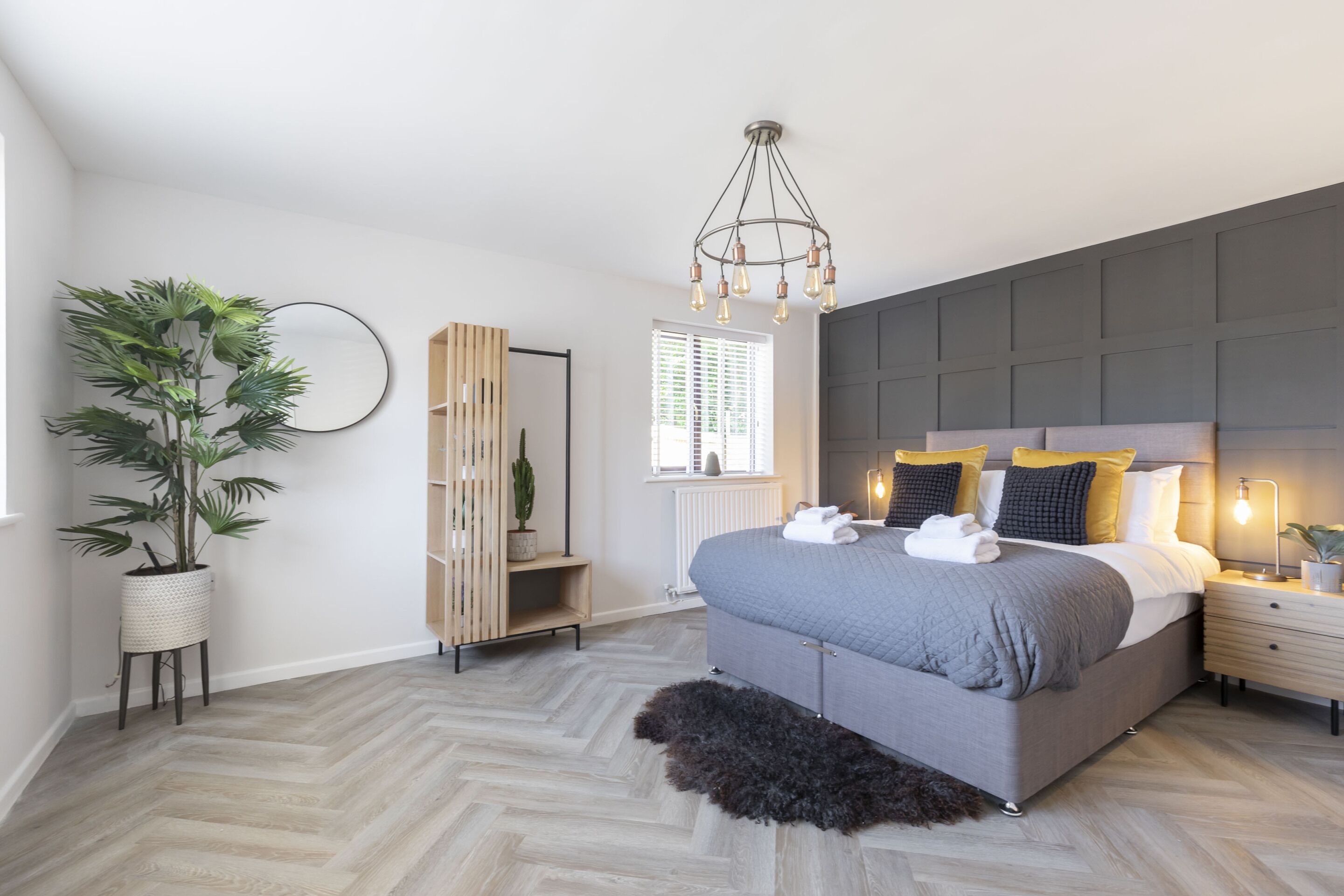 Een moderne slaapkamer met een groot bed, een houten garderobe, een potplant en een bijzondere lamp.