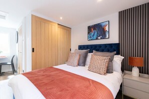 A modern bedroom with a large bed, a wooden wardrobe, a desk, and a wall-mounted TV.