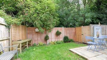A backyard with a wooden fence, a bench, a table with chairs, and a small garden area with plants.