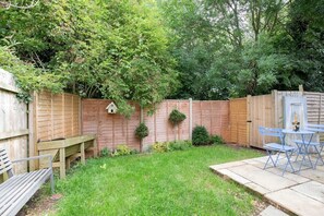 A backyard with a wooden fence, a bench, a table with chairs, and a small garden area with plants.